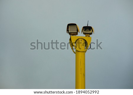 Yellow speed camera, used to take photos of cars that are exceeding the speed limit on the road. Cloudy sky in the background. Copy space to add text.
