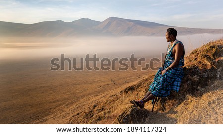 Young Masai Warrior sitting inside the crater of Ngorongoro park watching sunrise Royalty-Free Stock Photo #1894117324