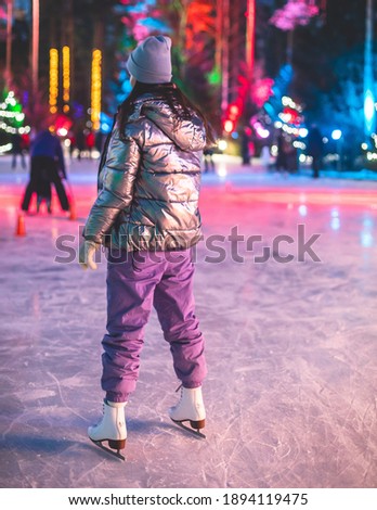 Girl ice skating on the ice rink arena with happy people around, concept of ice skating in winter, winter activities, holiday christmas time, with new year decoration and illumination