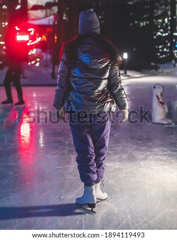 Girl ice skating on the ice rink arena with happy people around, concept of ice skating in winter, winter activities, holiday christmas time, with new year decoration and illumination