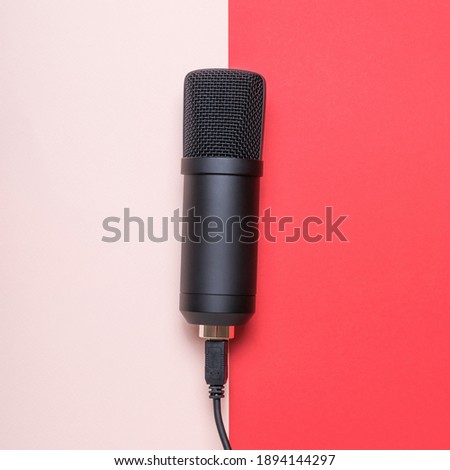 Microphone with connected wire on red and pink background. Sound recording equipment.