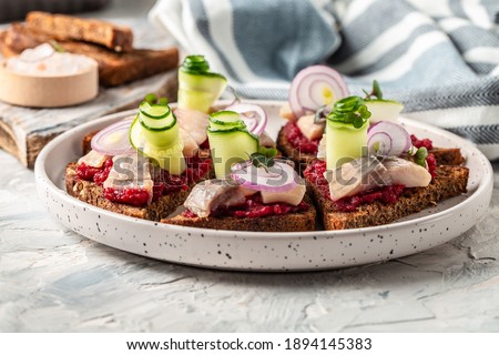 Tradition Danish open sandwich smorrebrod with herring, beetroot salad, green cucumber, onion and microgreen. Dark bread sandwich.