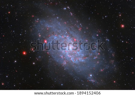 Galaxy M33 is set against a backdrop of dark space and multicolored stars. There are many little stars in the photo. A photograph of a real space object taken with a telescope. Soft focus.