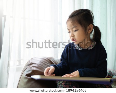 Asian children girl in blue dress reading book.Home school concept.