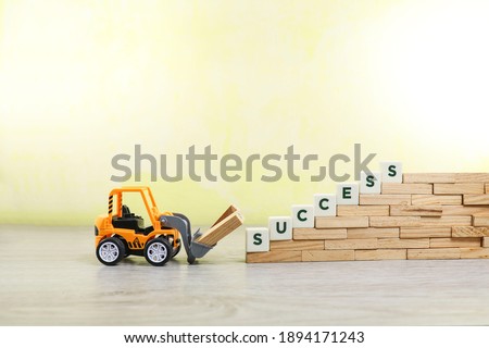 A toy bulldozer lifting wooden sticks with block letters on success arranged on the pile of wooden sticks 