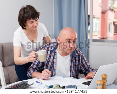 Smiling wife taking care of husband working at home with laptop. High quality photo