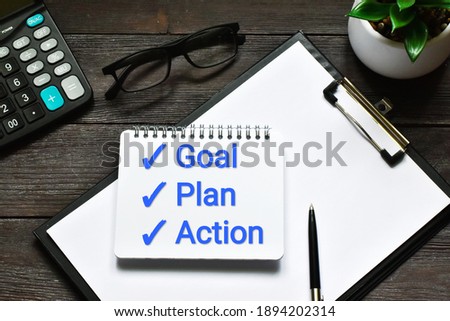Goal,plan, action text on notepad with office accessories, glasses and calculator on a wooden background. Business motivation, inspection concepts ideas.
