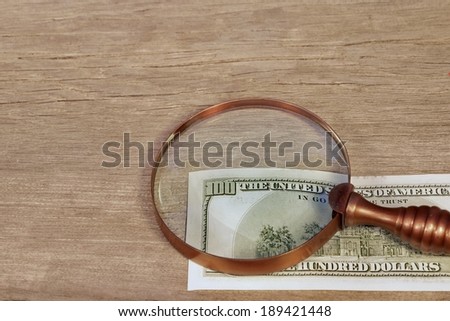 Hundred dollar bill under a old magnifying glass on timer board. Background with space for text or image