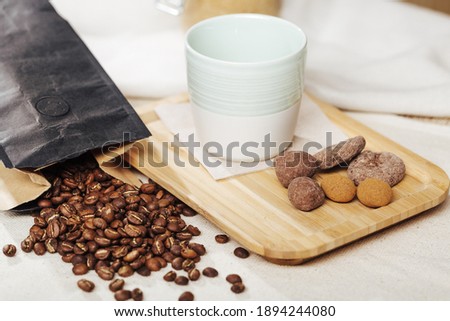 Ristretto coffee in ceramic cup with nuts wrapped in chocolate on a bamboo tray, decorated with fresh roasted coffee beans spilled from a paper bag onto a natural beige fabric.