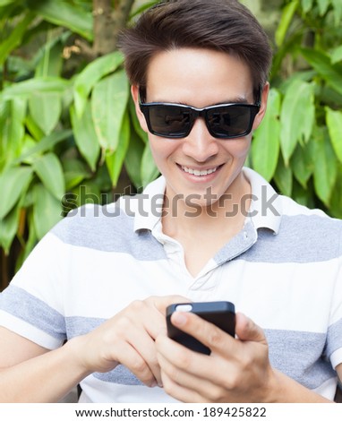 Smiling young man looking at his smart phone while text messaging.