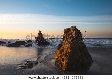 The wavy ocean hitting the rocky El Matador Beach gleaming under the sunset in Malibu, California