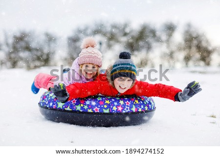 Active toddler girl and school boy sliding together down the hill on snow tube. Happy children, siblings having fun outdoors in winter on sledge. Brother and sister tubing snowy downhill, family time.