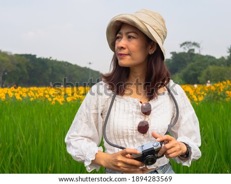 Portrait of 30-40s Asian women wearing white hats, wearing white shirts. Taking a picture with a toy camera In the park Full of green grass And sunflowers happily on a bright day With her holiday
