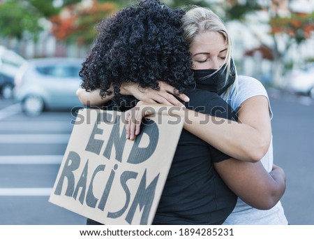 Young african woman hugging a caucasian woman after a protest - Northern woman with end racism bannner in her hands - Concept of no racism Royalty-Free Stock Photo #1894285231