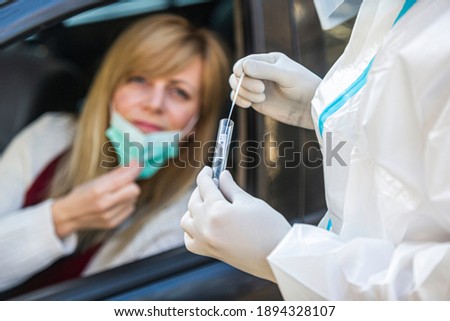Woman sitting in car, waiting for medical worker to perform drive-thru COVID-19 test, taking nasal swab sample through car window, PCR diagnostic for Coronavirus, doctor in PPE holding test kit.