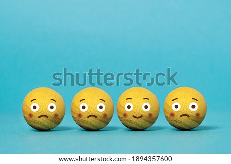 Wooden balls with emoticons of sadness and happiness. Concept of mood change. Blue background
