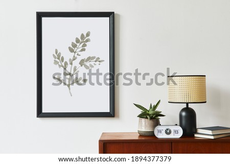 Retro modern compositon of living room interior with design teak commode, black mock up poster frame, clock, plant, decoration, white wall and personal accessories. Template.