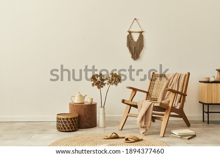 Stylish interior design of living room with wooden armchair, coffee table, furniture, rattan decoration, dried flowers and elegant personal accessories. Copy space white wall. Template. Royalty-Free Stock Photo #1894377460