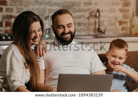 A close up photo of the happy family. A smiling father is working remotely on a laptop while his son and wife are staring at the screen. Dad is working online on a computer with relatives at home