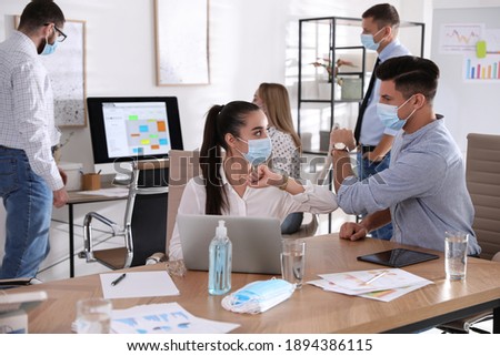Coworkers with protective masks making elbow bump in office. Informal greeting during COVID-19 pandemic Royalty-Free Stock Photo #1894386115