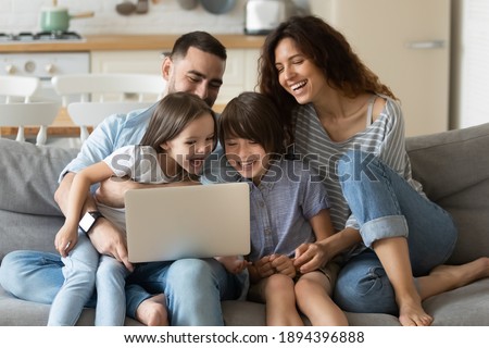 Close up happy parents with daughter and son using laptop sitting on couch at home. Smiling mother, father and cute children looking at laptop screen using video call. Family having fun with computer. Royalty-Free Stock Photo #1894396888