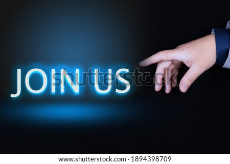 JOIN US text is a word written in neon letters on a black background pointed to by a hand with a person's index finger.
