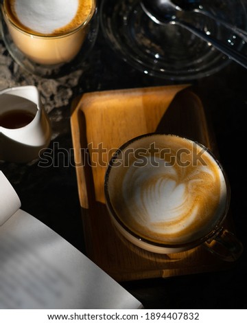 Latte coffee and set of morning drinking with book on glass table with light and shadow shading in to view. Dark emotion of morning. Vertical picture.