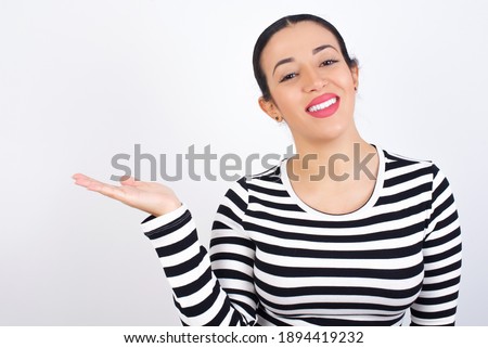Young beautiful woman wearing stripped t-shirt against white background smiling cheerful presenting and pointing with palm of hand looking at the camera.