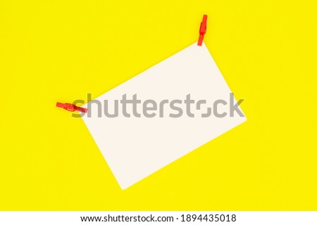 Blank white paper with red clothespins on a yellow background. Holiday marketing, greeting card, invitation, electronic newsletter concept.
