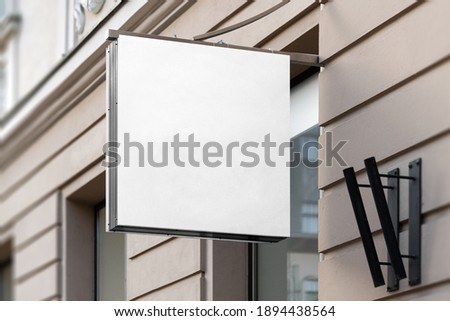 Blank square sign mockup in the urban environment, on the facade, empty space to display your store sign or logo