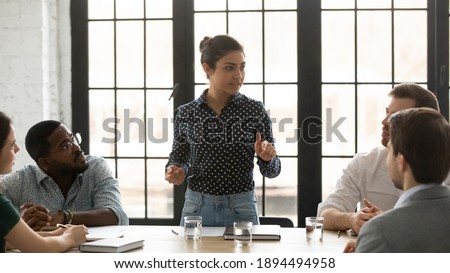 Indian project leader and diverse mates gathered in boardroom brainstorming making sales analysis. Female business trainer teach multiracial apprentices during corporate training. Mentoring concept Royalty-Free Stock Photo #1894494958