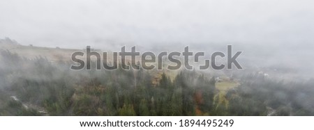 Rainy foggy and gray weather in the mountain valley of the Carpathians in Ukraine in small village Aerial panoramic drone shot