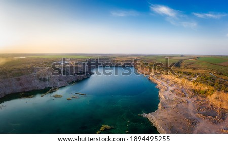 Old flooded stone quarry with large stones in the evening warm bright light covered with small dry plants in picturesque Ukraine. Aerial panoramic drone shot