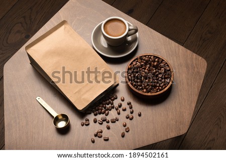 Blank coffee packaging on a wooden table, with pot, coffee seeds bowl, copper spoon, cup with coffee on a wooden background, coffee packaging mockup with empty space to display your branding design.