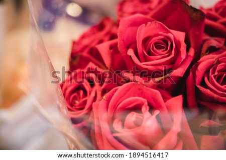 Close up view of red roses bouquet in wrapping paper plastic on the foreground.