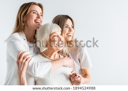 three generation of positive women smiling while hugging isolated on white Royalty-Free Stock Photo #1894524988