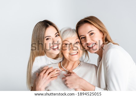 three generation of positive women smiling while looking at camera and hugging isolated on grey Royalty-Free Stock Photo #1894525015