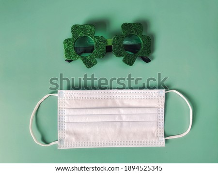 Saint Patrick Day celebration. Medical face mask and party glasses in green background. Flat lay, top view. New normal for COVID 19. Medicine concept.