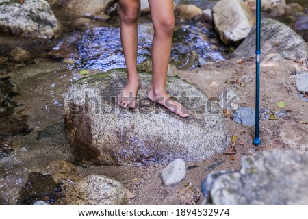 Child barefoot feet standing on rocks by the clear water at forest creek . Adventure on summer day in nature. Unrecognizable people .