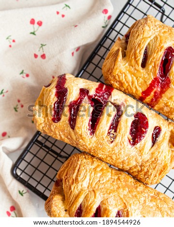 Three strudels of baking dough on a black grate napkin with cherry print