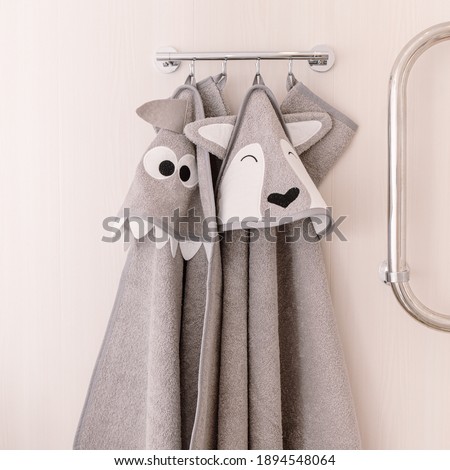Two grey hooded baby towels hang in bathroom. Embroidery shark and wolf