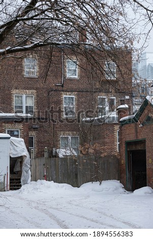 Quebec city back alley during winter, with snow and trees. Bricks building.