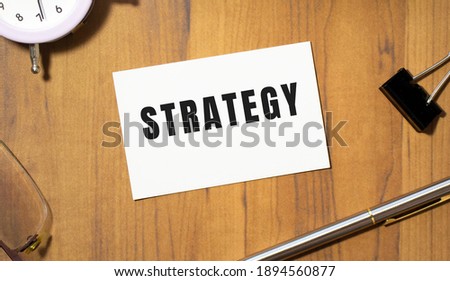 A business card with the text STRATEGY lies on a wooden office table among office supplies. Business concept.