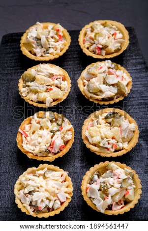 Salad tartlets with pineapple on a black wooden board on a gray concrete background. Vertical photo