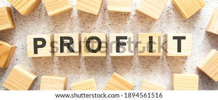 The word PROFIT consists of wooden cubes with letters, top view on a light background. Work space.