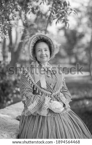 Woman in victorian dress walking in the park. Vintage fashion. White and black photo
