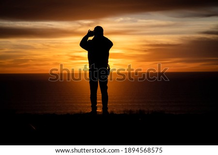 Silhouette of a man looking out at a sunset or sunrise taking a cell phone picture 