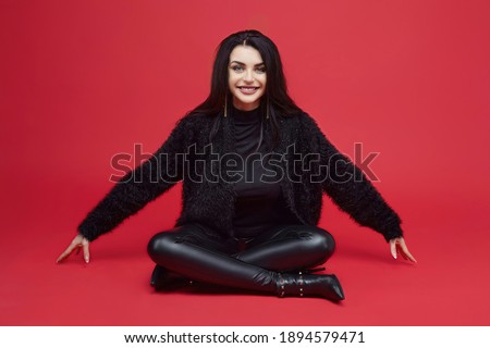 attractive brunette with long hair sitting in the Studio on a red background