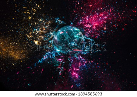 explosion of a glass ball with colored lights, black background. high speed photography.