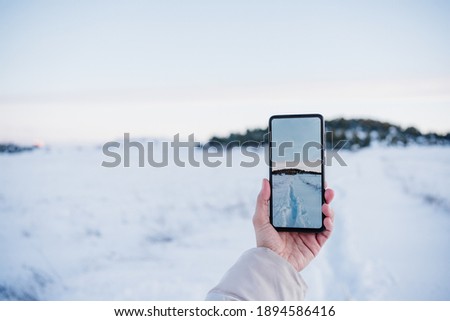 close up of backpacker woman hiking in snowy mountain taking a picture of landscape with mobile phone.winter season. nature and technology